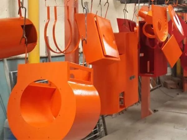 Boyanmak üzere asılmış turuncu fan gövdeleri ve makine parçaları